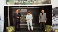 Zwei Soldaten und eine Frau stehen vor einer Werbetafel. Die Frau trägt eine 3D-Brille.