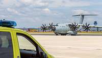 Ein A400M mit laufendem Triebwerk steht auf einem Rollfeld. Davor ein Rettungswagen.