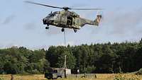 Ein Hubschrauber schwebt über einem Lastwagen und hebt eine Last an.
