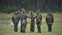 Mehrere Soldaten stehen auf einem grünen Feld. Zwei von ihnen legen ihre Hand auf eine gesenkte Fahne. 