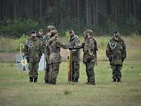 Vereidigung auf dem Übungsplatz Mehrere Soldaten stehen auf einem grünen Feld. Zwei von ihnen legen ihre Hand auf eine gesenkte Fahne.