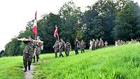 Pilger mit einem Kreuz und Fahne auf schmalem Pfad bei 2. Nationale Militärwallfahrt Flüeli-Ranft