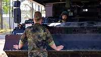 Eine Soldatin sitzt in einem Panzer, ein zweiter Soldat steht vor dem Panzer und bespricht sich mit ihr 