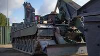 Eine Soldatin sitzt in einem Panzer und nimmt mit einem Greifarm die Gefechtsfeldbrücke auf