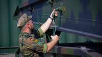 Ein Soldat steht vor Brückenelementen und löst einen Spanngurt