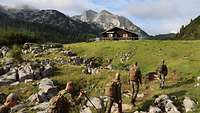 Auf einem grünen Hochplateau gehen mehrere Soldaten in Reihe Richtung Gipfel. 