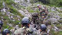 Drei Jugendliche in Flecktarn schauen an einer Felswand hinauf, zwei sind bereits hinaufgeklettert.