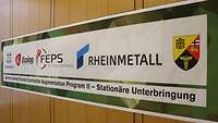 Ein farbiges Banner mit nebeneinander stehenden Wappen und Unternehmenslogos 