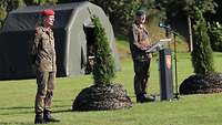 Ein Soldat steht an einem Rednerpult mit Mikrofon, ein zweiter steht mit Abstand neben ihm.