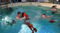 A person tries to put on a red suit in the water.