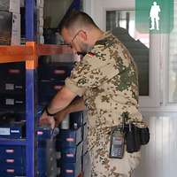 Ein Soldat steht vor einem Regal mit Alarmanlagen. Diese sind in kleine Kartons verpackt