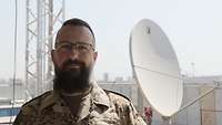 Ein Soldat sieht in die Kamera. Im Hintergrund hängt eine Satellitenschüssel