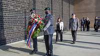 Zwei Soldaten tragen einen Kranz, eine Zivilistin und ein Soldat laufen hinterher