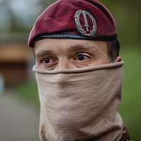 Ein Soldat mit Tuch im Gesicht und weinrotem Barett im Porträt