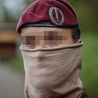 Ein Soldat mit Tuch im Gesicht und weinrotem Barett im Porträt