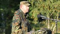 Ein Soldat steht hinter einem getarnten Rednerpult und spricht in ein Mikrofon.
