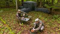 Zwei Soldaten vor einem Zelt mit Anbauten und Zubehör in einem Wald