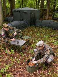 Zwei Soldaten vor einem Zelt mit Anbauten und Zubehör in einem Wald