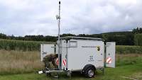 Ein Mann in Uniform beugt sich über die Achse eines Anhängers mit einer Antenne und Bundeswehr-Aufdruck.