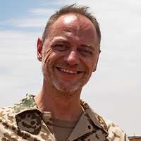 Eine Soldatin und ein Soldat stehen im Feldlager auf einer roten Sandpiste