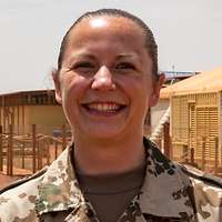 Eine Soldatin und ein Soldat stehen im Feldlager auf einer roten Sandpiste