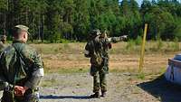 Ein Soldat mit weißen Armbinden gibt die letzten Instruktionen bevor das Schießen beginnt. Er deutet mit dem Finger auf etwas