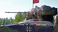 In einem Panzer sitzen Soldaten und eröffnen das Feuer, eine rote Fahne weht auf dem Panzer