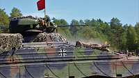 Ein Soldat steht im Panzer und beobachtet und feuert die Bordmaschinenkanone ab