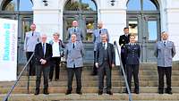 Auf der Treppe vor einem Gebäude stehen Soldaten und Zivilisten nebeneinander für ein Gruppenfoto.