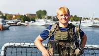 Ein junger Mann steht bekleidet mit einer Kampfmittelweste im Hafen.