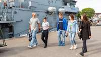 Eine Gruppe von Menschen geht an Marineschiffen vorbei