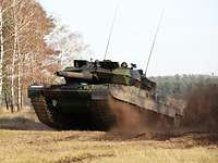 Ein Kampfpanzer fährt über eine sandige Freifläche und scheint bei voller Fahrt abzuheben. 