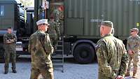Mehrere Soldaten stehen vor einem Fahrzeug mit Containeraufsatz, zwei betreten über eine Leiter den geöffneten Container.