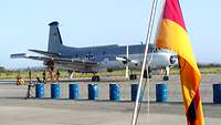 Ein Propellerflugzeug steht hinter einer Deutschlandfahne.