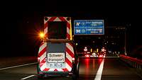 Ein schwerer Lkw fährt im Dunkeln auf der Autobahn voraus, ein Absicherungsfahrzeug folgt ihm.