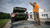 Ein Soldat mit Signalweste steht auf einem Tieflader und gibt dem Panzerfahrer Rangierzeichen.