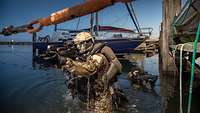 Zwei KSM-Soldaten mit Waffen im Anschlag kommen aus dem Wasser neben einem Bootssteg