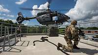 Zwei bewaffnete HSG-Soldaten knien auf dem Dach eines Gebäudes, neben dem ein Hubschrauber schwebt