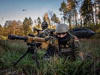 EGB-Kräfte Ein EGB-Soldat liegt mit Maschienengewehr im Anschlag im Gelände, im Hintergrund ein Hubschrauber am Boden