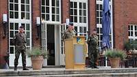 Ein Soldat steht am Rednerpult. Links und Rechts davon steht ebenfalls ein Soldat.