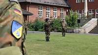Am Ärmelabzeichen eines Soldaten vorbei sieht man zwei Soldaten mit militärischem Gruß, die sich gegenüber stehen.