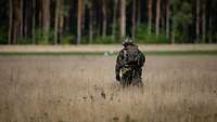 Ein Soldat mit einem Rucksack läuft durch ein Feld.