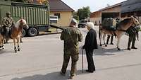 Ein Soldat und eine Frau schauen sich einen Soldaten an, der auf einem Pferd sitzt. Rechts ein beladenes Maultier.