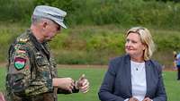 Ein Soldat und eine Zivilistin in graublauem Hosenanzug und weißem Shirt sprechen miteinander.