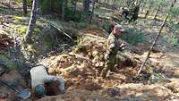 Soldaten bewegen im Wald mit Schaufeln das Erdreich.