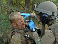Eine Sanitäterin mit blauen Gummihandschuhen leuchtet in die Augen eines verwundeten Soldaten.