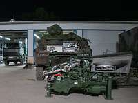 Ein Radpanzer steht vor einer Halle, davor ist der ausgebaute Motorblock abgestellt.