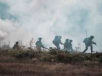 Sechs Soldaten laufen über eine Freifläche, im Hintergrund ist dichter Rauch zu sehen.