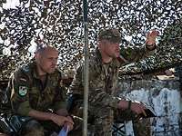 Zwei Soldaten sitzen nebeneinander unter einem Tarnnetz.
