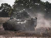 Ein Panzer fährt schnell durchs Gelände, Staub wirbelt auf.